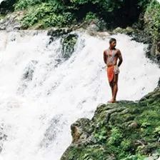 A man in traditional dress standing beside a small waterfall in Panama, a featured new tour destination